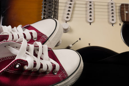 Red sneakers and blurred guitar in background. Close up, selective focus. Rock and Roll fashion...