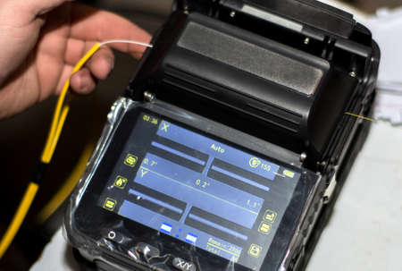Engineer splicing fiber optic cable with Optical Fiber Fusion Splicer with tool with display. Close up, selective focus. Modern and fast internet and network concept.の写真素材