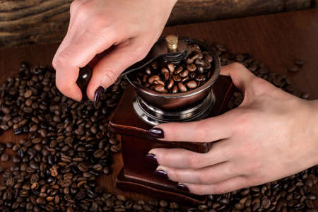 Female hands grinding roasted coffee beans in old retro mill. Retro and Vintage food and drink concept. Close up, selective focusの写真素材