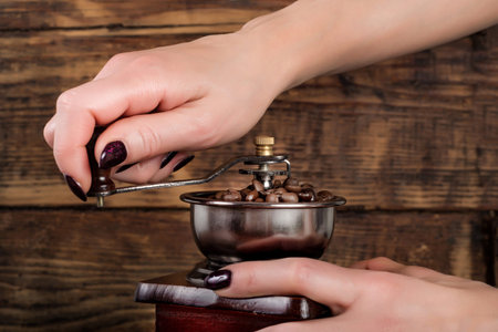 Female hands holding and grinding roasted coffee beans on wooden background. Retro and Vintage food...