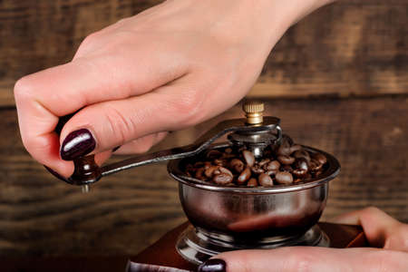 Woman hand grinding coffee roasted beans in retro mill and wooden background. Retro and Vintage concept drink and food. Close up, selective focusの写真素材