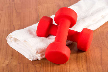 Red fitness dumbbell on white towel at wooden hame floor. Sport and recreation conceptの写真素材