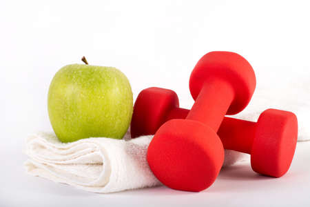 Red dumbbell and green fresh apple on towel on white background in studio. Sport, fitness, diet and health food conceptの写真素材