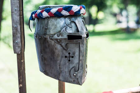 Iron helmet of the medieval knight on wooden stand with red, blue and white ribbon in nature. Middle ages armor concept. Close up, selective focusの写真素材