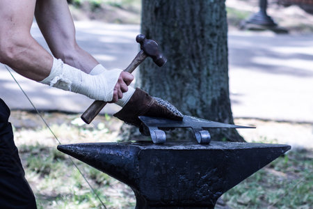 Process of making medieval ax weapon. Blacksmith hands manually forging metal on anvil with hammer...