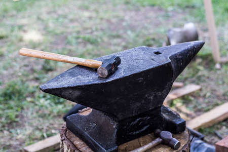 Old anvil on wooden log and blacksmith hammer tool outdoor. Close up, selective focusの写真素材