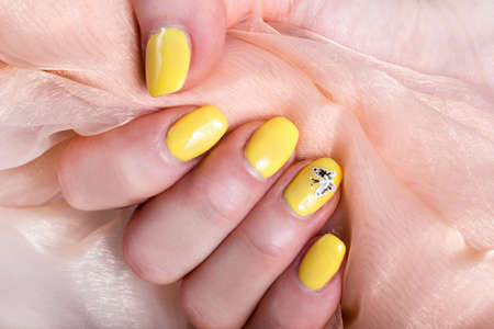Female with yellow nails manicure polish holding soft pink silk fabric. Woman beauty concept. Close up, selective focusの写真素材