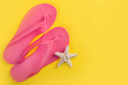 Pink sandal flip flops and starfish isolated on yellow background. Empty space for text and design. Summer vacation concept. Top viewの写真素材