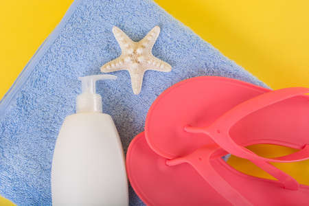 Pink sandal flip flop on blue towel and suntan cream lotion and starfish on yellow background. Summer vacations concept, close up, top viewの写真素材