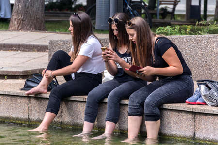 Niska Banja, Serbia - July 02, 2018 Young happy girls relaxing legs in water and looking in phone in spa. Vacation and enjoyment of the summer conceptのeditorial素材