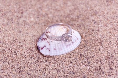 Wedding diamond engagement ring on sea shell and sandy blurred and soft background. Jewelry concept....