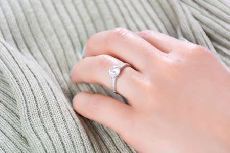 Female hands with diamond engagement wedding ring on fabric texture background. Jewelry and beauty concept. Close up, selective focusの写真素材