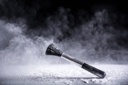 Brush for makeup with powder and dust fog explosion in air on black background and white dust on...