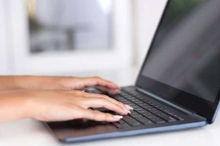Young female hands working and typing on laptop keyboard in office. Modern work and job concept. Blurred windows and background. Close up, selective focusの写真素材