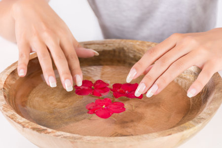 Beautiful female natural manicure nails and wooden bowl with water and red flower. Spa treatment for hands concept. Close up, selective focusの写真素材