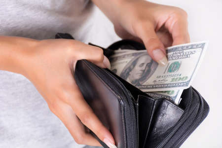 Female hand hold a black purse with America dollars and pay. Economy and shopping concept. Close up, selective focusの写真素材