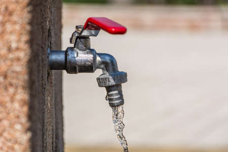 Faucet with red handle and open water outdoor on sunny summer day. Save water concept. Close up, selective focusの写真素材