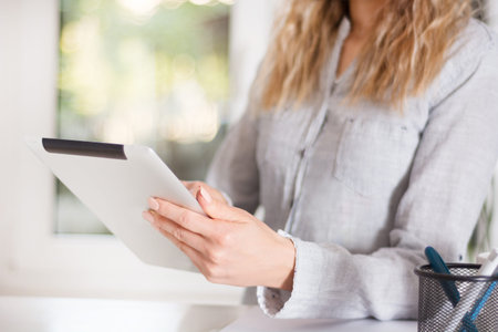 Elegant business woman holding digital tablet at modern office and working. Girl in shirt sitting on...