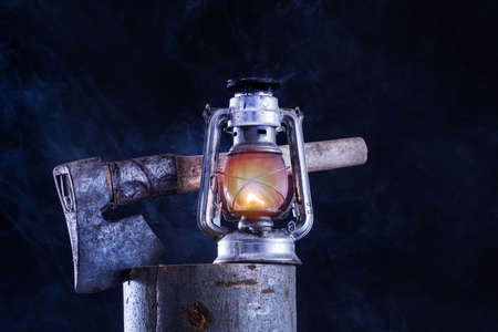 Old gas lamp burning and ax in lumber log and foggy smoke dark night background. Rust metal lantern with corrosion. Horror and Halloween conceptの写真素材