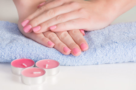 Gently pink gel nails polish on woman hands on blue towel and pink candles on desk in studio....
