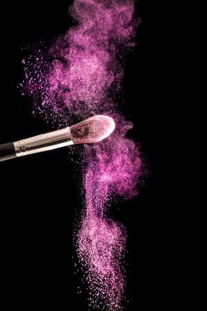 Make up brush with purple dust powder explosion isolated on black background. Beauty and fashion concept. Close up, selective focusの写真素材