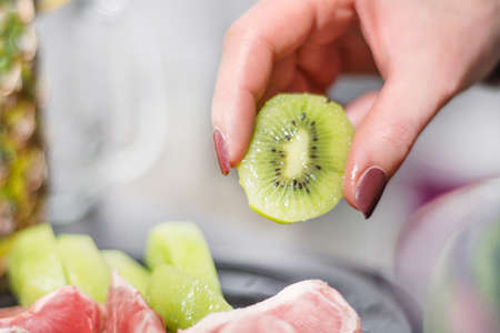 Green peeled kiwi fruit holds woman hand. Fruit healthy salad and food concept. Beautiful light blurred background. Close up, selective focusの写真素材