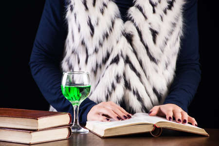 Young woman reading book in dark and old library and drinks absinthe or green fairy drink. Artist and inspiration concept image. Close up, selective focusの写真素材