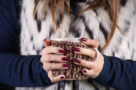 Girl holding cup of hot drink tea in hands and woman has red wine color manicure on finger nails....