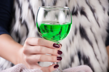 Glamorous woman holding in hand Absinthe green drink. Girl with red wine color manicure. Woman in...