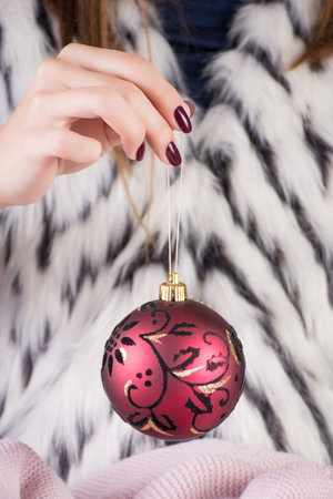 Girl hand holding Christmas ball decoration in hands with wine color manicure on fingernails. Woman...
