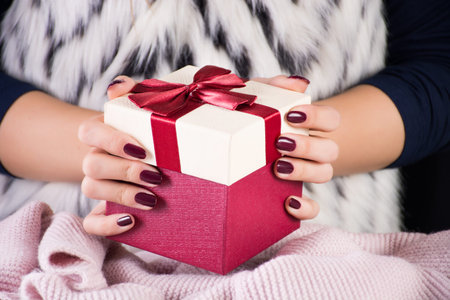 Girl holding red gift present box with tie bow in hands. Woman in fur waistcoat with zebra pattern....