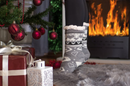 Girl feet in Christmas socket standing on fingers near fireplace and decorated Xmas tree. Christmas...