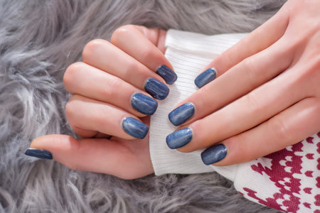 Girl hands with navy blue nail polish color on winter sweater and gray furry background. Manicure...