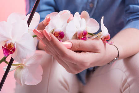Woman with pink spring manicure on nails polish holds orchids flowers in hands. Manicure and beauty concept. Close up, selective focusの写真素材