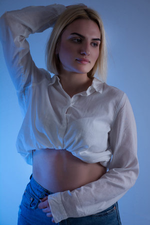 Fashion portrait of beautiful woman in white shirt with bare stomach and blue background in studio....