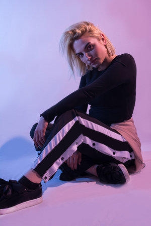 Girl in sports tracksuits sitting down on colorful lights and background in studio and posing. Sport...