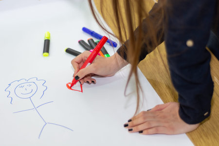 Woman hand with red felt pen drawing heart on big white paper with stickman on desk in classroom....