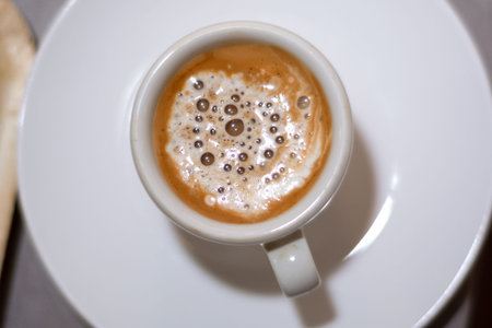 Top view of espresso coffee in a white cup on a saucer. Brown coffee with milk and bubble. Close up,...