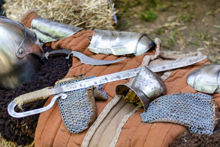 A medieval knights equipment, sword and iron protective gloves on desk outdoor. The historical and medieval item for battle. Close up, selective focusの写真素材