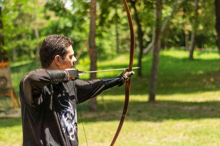 Nis, Serbia - June 16. 2019: Archer with bow shoot arrow in the forest on knight festival in a traditional suit. Bowman before shooting from a longbow. Close up, selective focusのeditorial素材