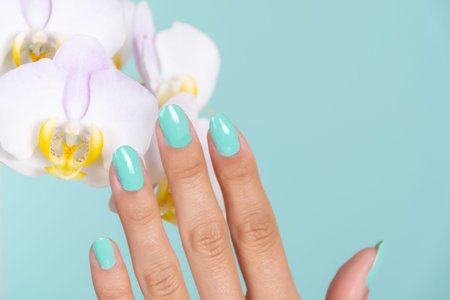Young girl hand with a turquoise color manicure on nails and light lilac orchids flower isolated on...