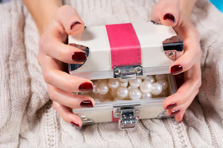 Young girl hands opening small jewelry case with pearls necklace. Women suitcase box in female hands with brown manicure on woolen sweater background. Close up, selective focusの写真素材