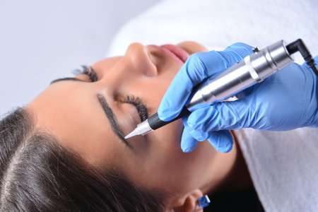 Applying permanent make up on eyebrows in beauty studio on a young woman. Cosmetologist hand...