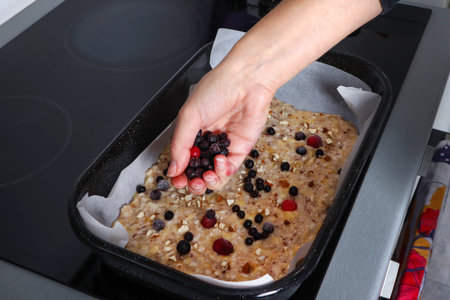 Woman hand puts berries ingredients on vegetarian sweet fruit pizza with berries. Fresh pizza in a...