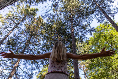Girl arms raised enjoying the fresh air in green pine tree forest on a summer day. Relaxation in nature and freedom conceptの写真素材