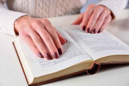Woman hand on an open book and brown gel nails polish on fingers. Manicure and beauty concept