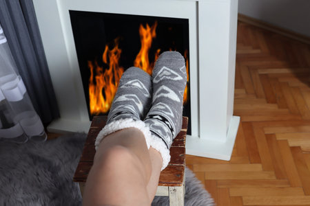Young girl sitting in front of the fireplace and warming legs on fire. Woman wears wool socks....