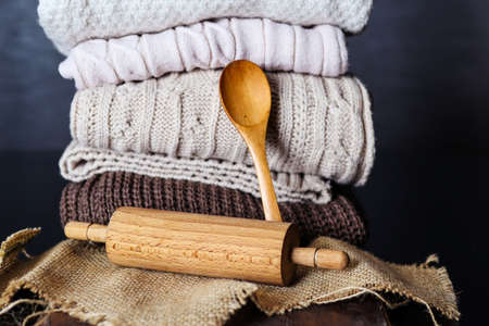 Wooden rolling pin and spoon on desk and piles of sweaters in the background at home. Copy space for design or textの写真素材