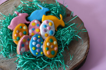 Cute homemade colorful cookies in the shape of eggs and rabbit on log and grass. Easter holiday...