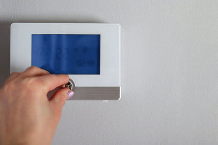 Female hand adjusts and regulates the room temperature on the smart switch on the wall at home. Copy...